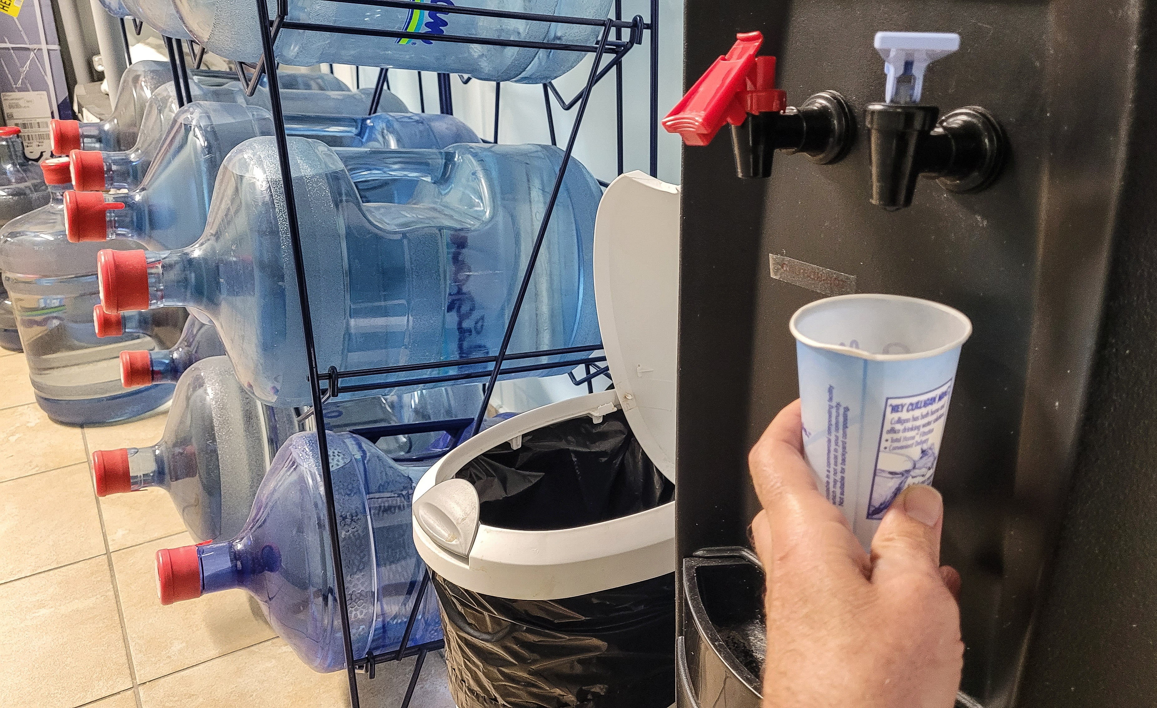 person drinking from a water cooler with rows of bottles behind it